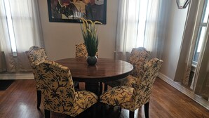 Un comedor con una mesa redonda de madera rodeada de sillas con estampado floral, un cuadro en la pared y un reloj.