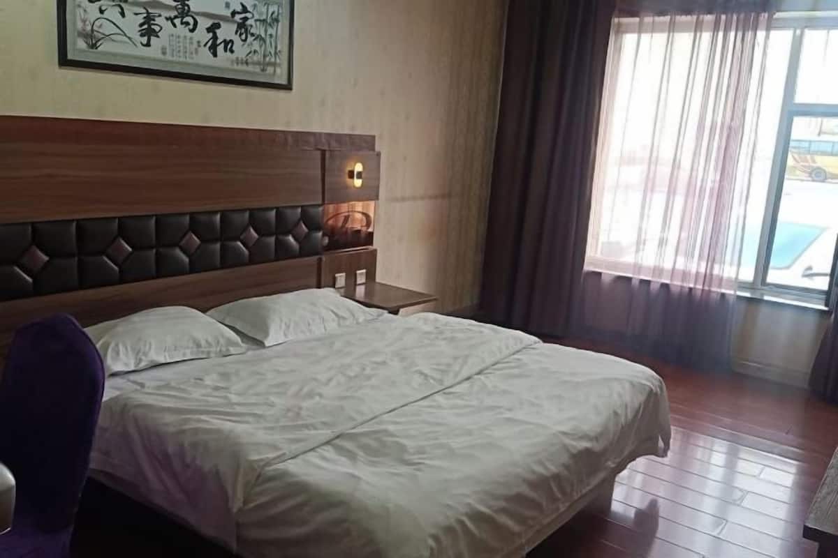 A hotel room with a large bed, a wooden headboard, a nightstand, and a window with curtains.