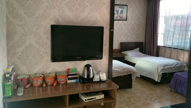 A hotel room with a flat-screen TV, two beds, a wooden TV stand with various items, and a window with curtains. - Deli Business Hotel (Baicheng)