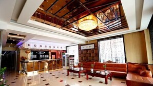 Un hall d’hôtel comprenant un comptoir d’accueil, un espace salon avec des canapés, un lustre et un sol carrelé.
