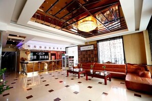 A hotel lobby with a reception desk, a seating area with sofas, a chandelier, and a tiled floor.