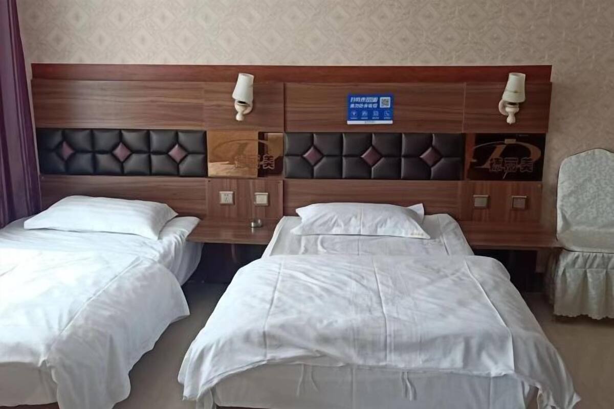 A hotel room with two beds, a wooden headboard with a padded section, a small table, and a chair.