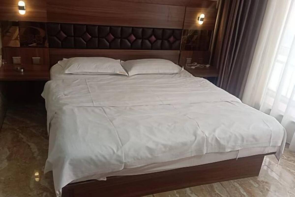 A hotel room with a wooden headboard, a bed with white linens, a nightstand with a lamp, and a mirror.