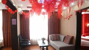 A hotel room with a sofa, a chair, a small table, and a bed. - Deli Business Hotel (Baicheng)