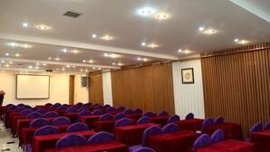 A conference room with rows of tables and chairs, a projector screen, and a wooden panel wall. - Deli Business Hotel (Baicheng)