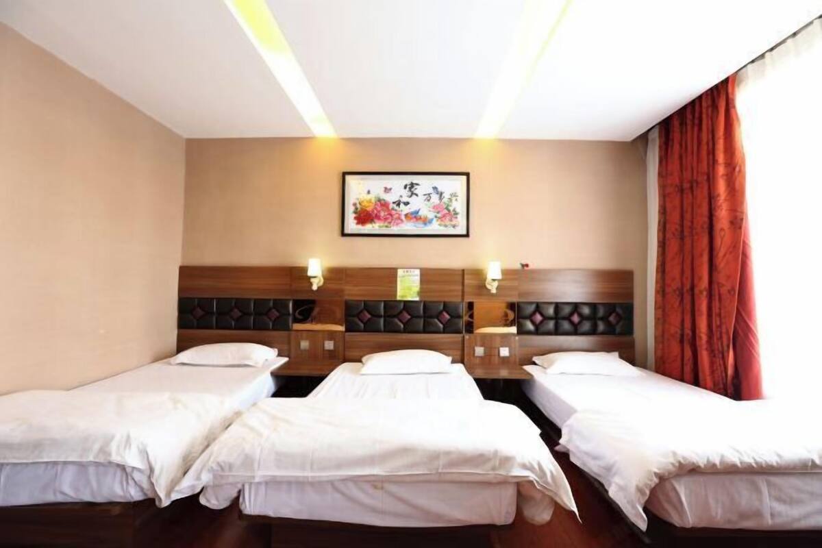 A hotel room with three single beds, a wooden headboard, a wall-mounted artwork, and a red curtain.