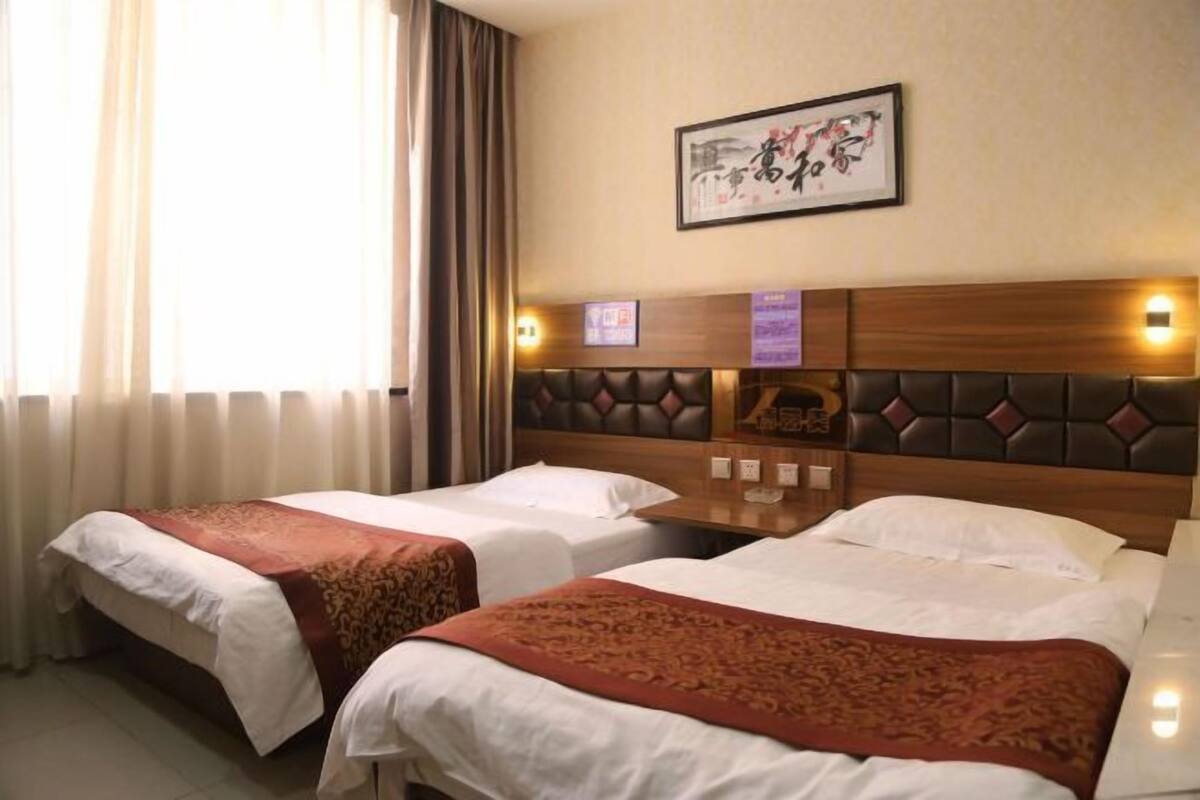 A hotel room with two beds, a wooden headboard, a framed artwork on the wall, and a window with curtains.