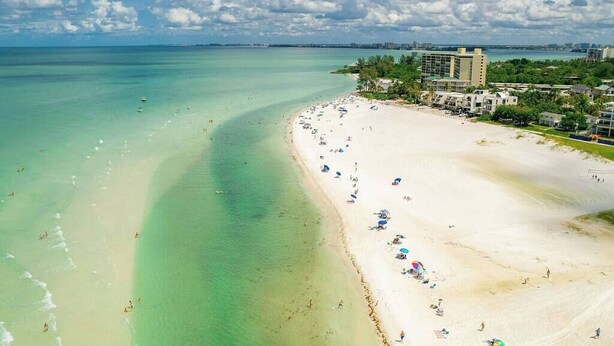 Una playa con agua turquesa cristalina, arena blanca y una fila de sombrillas.