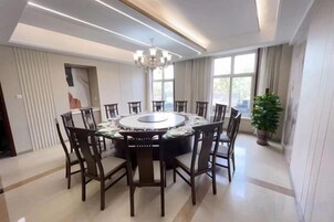 Un comedor con una mesa redonda rodeada de sillas, una araña y ventanas amplias.