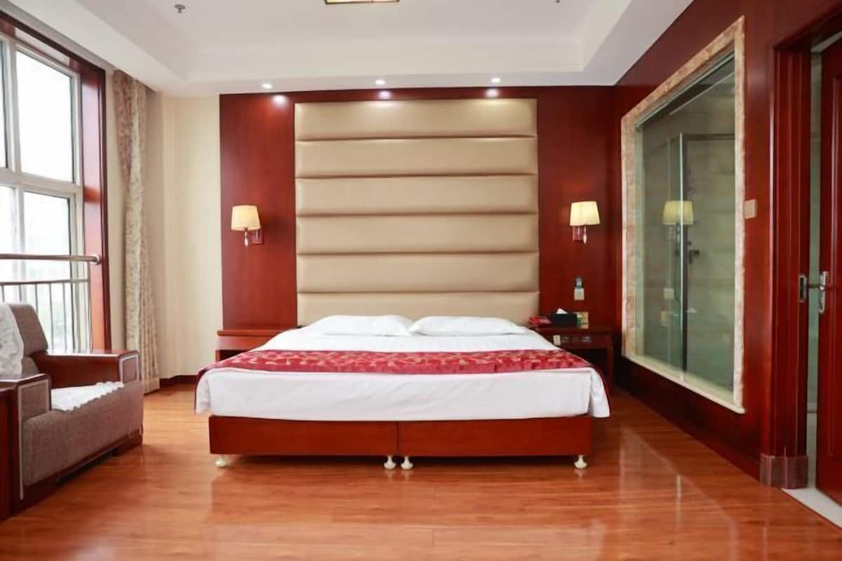 A hotel room with a large bed, two bedside lamps, a nightstand, a chair, and a large window.