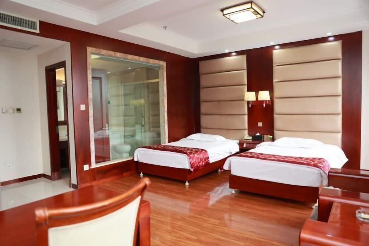 A hotel room with two beds, a glass shower enclosure, wooden flooring, and a wooden desk.