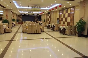 Un salón de banquetes con varias mesas redondas y sillas, un escenario al frente y un patrón de pared a cuadros.