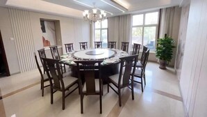 Un espace repas avec une table ronde entourée de chaises, un lustre et de grandes fenêtres.
