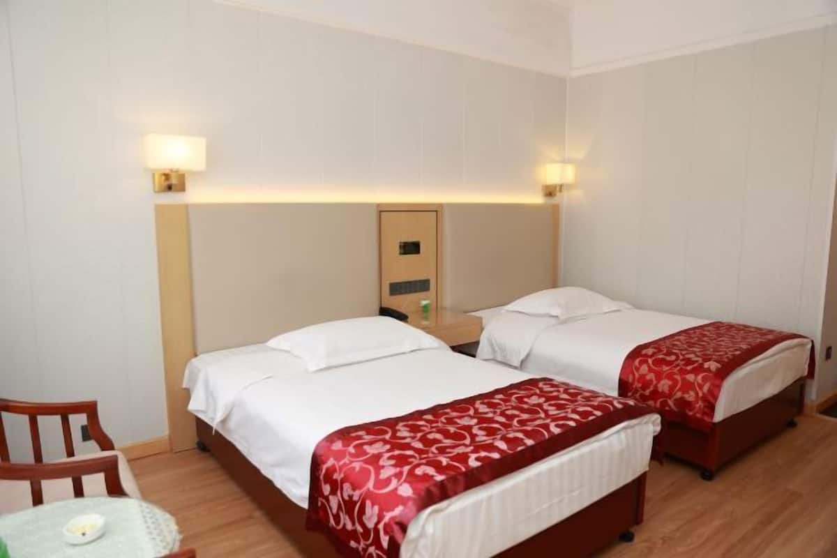 A hotel room with two beds, a chair, a table, and a nightstand with a lamp.