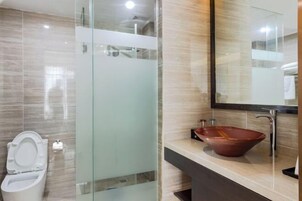 Un baño moderno con ducha acristalada, inodoro blanco y un espejo grande sobre un mostrador beige con un lavamanos rojo de diseño.