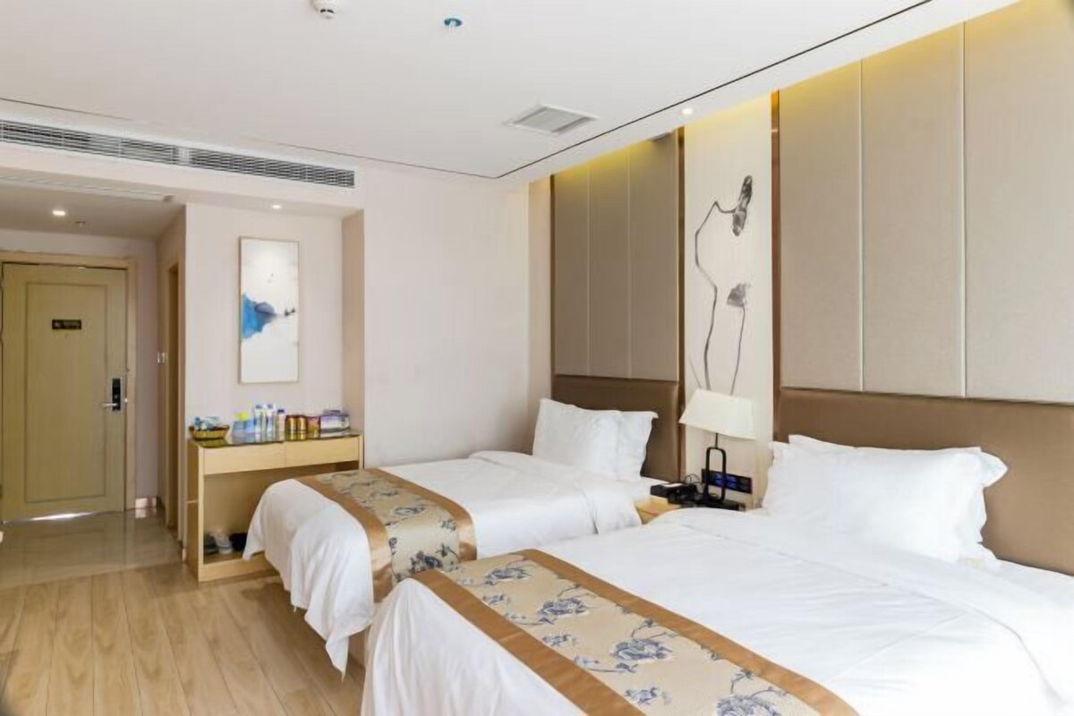 A hotel room with two beds, a wooden floor, a desk with toiletries, and a wall-mounted artwork.