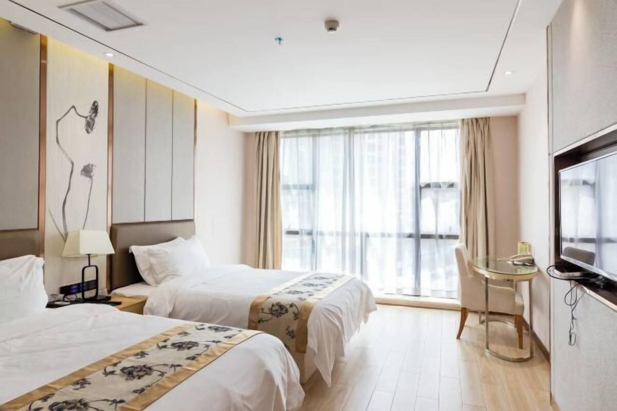 Hotellihuone, jossa on kaksi sänkyä, televisio, pieni pöytä ja suuri ikkuna.