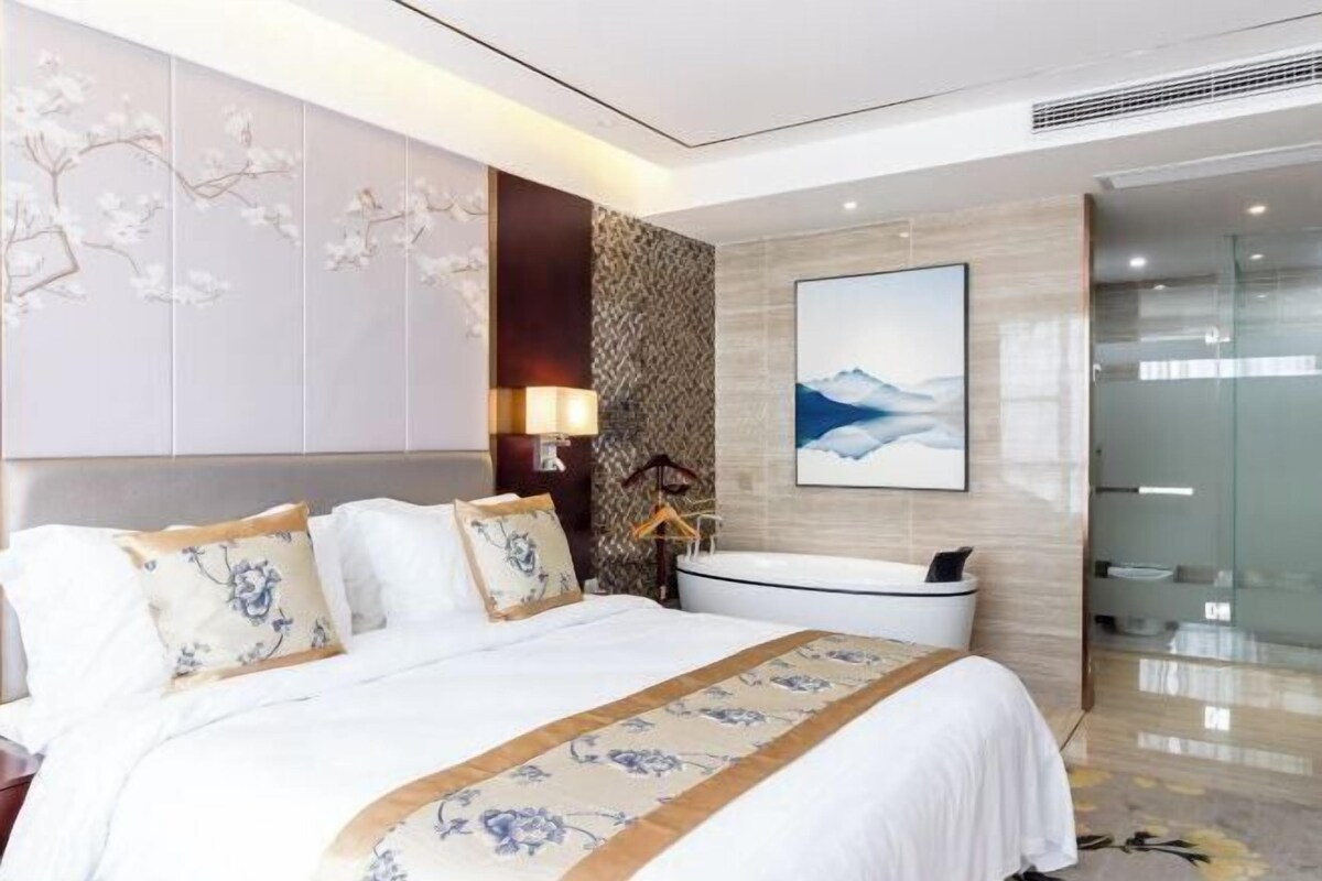A modern hotel room with a large bed, a bathtub, and a wall-mounted artwork.