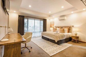 A modern hotel room with a large bed, a desk, a chair, and a view of the outdoors.