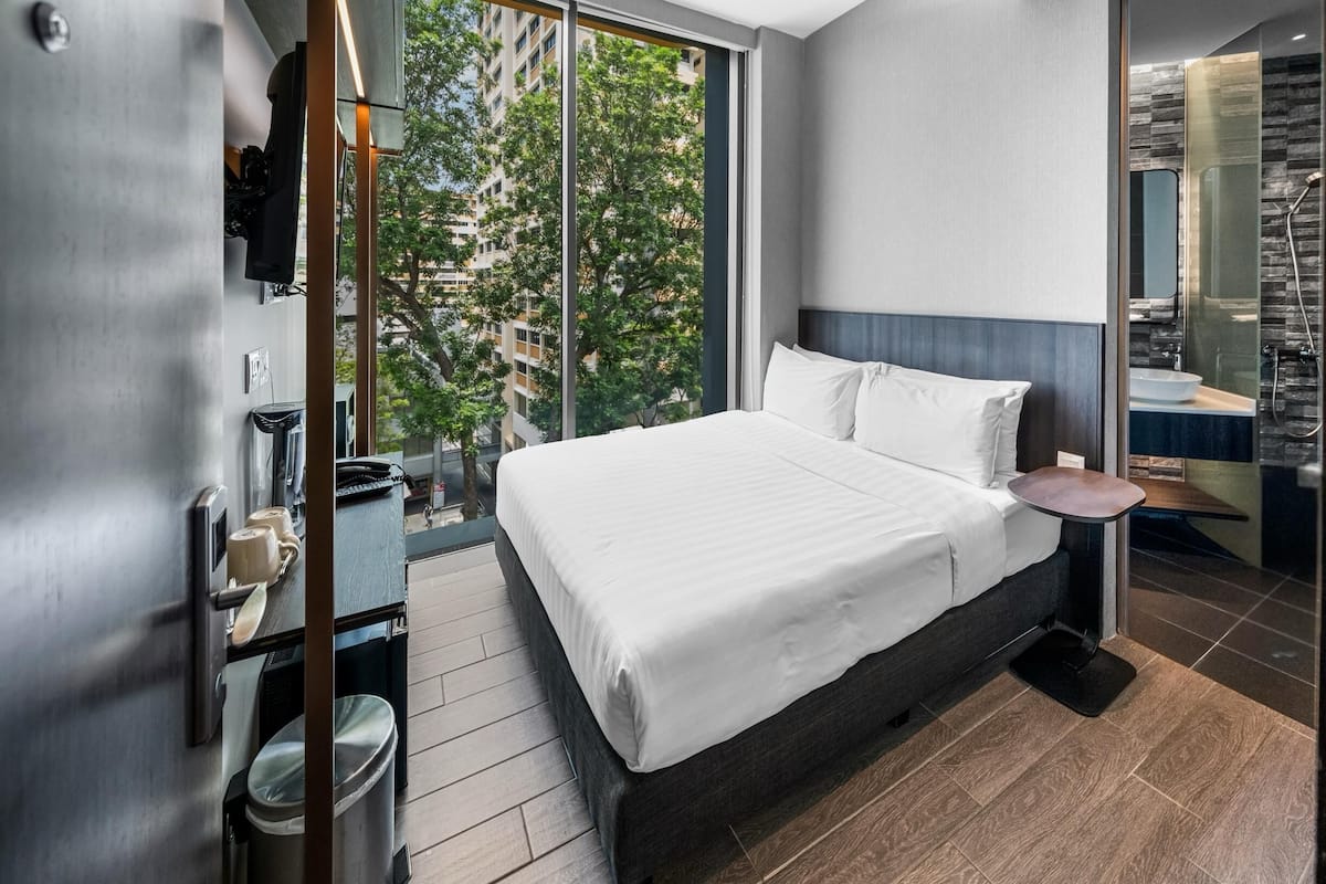 A modern hotel room with a large bed, a small bedside table, a built-in shower, and a view of the city.