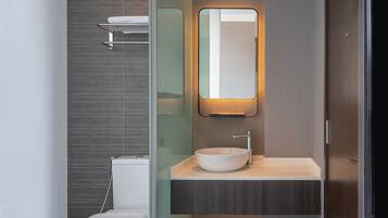 A modern bathroom with a glass partition, a white toilet, a vessel sink, and a mirror with integrated lighting.