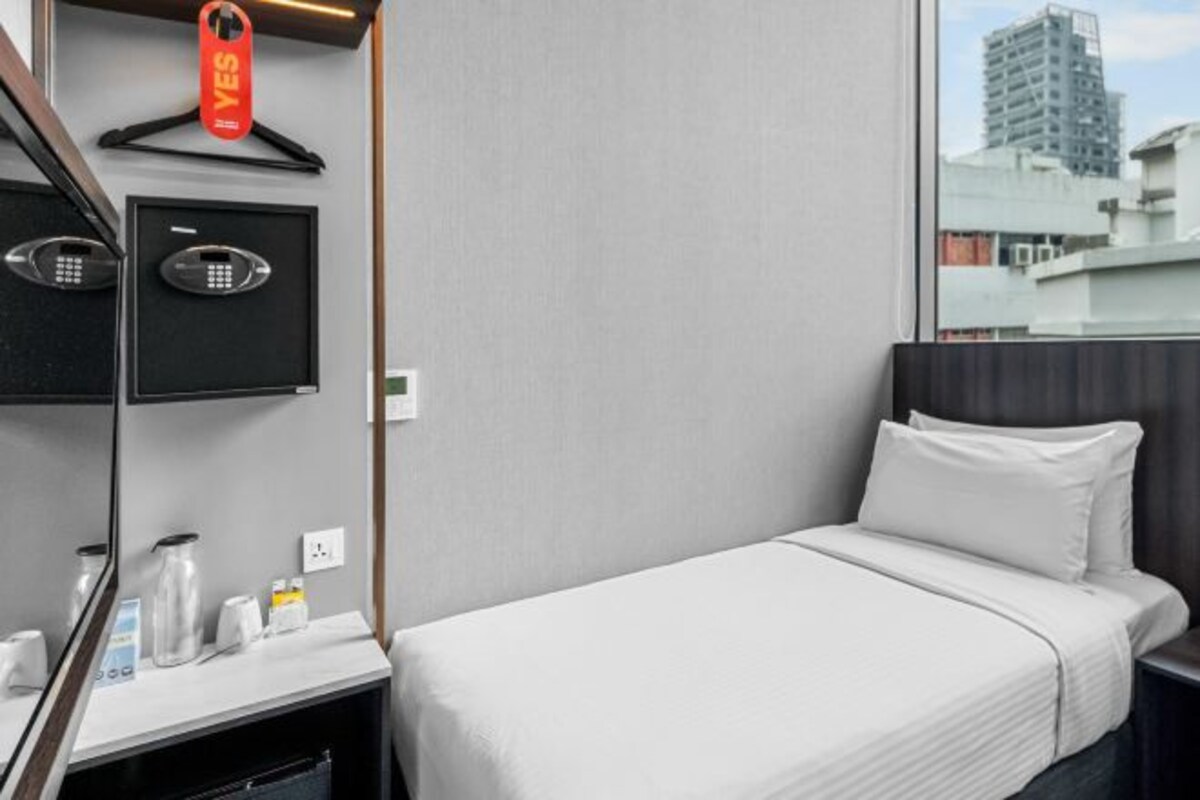 Habitación de hotel con cama, escritorio, teléfono, espejo y ventana con vista a la ciudad.