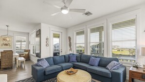 Ein modernes Wohnzimmer mit einer Eckcouch, einem runden Couchtisch und einem Deckenventilator.
