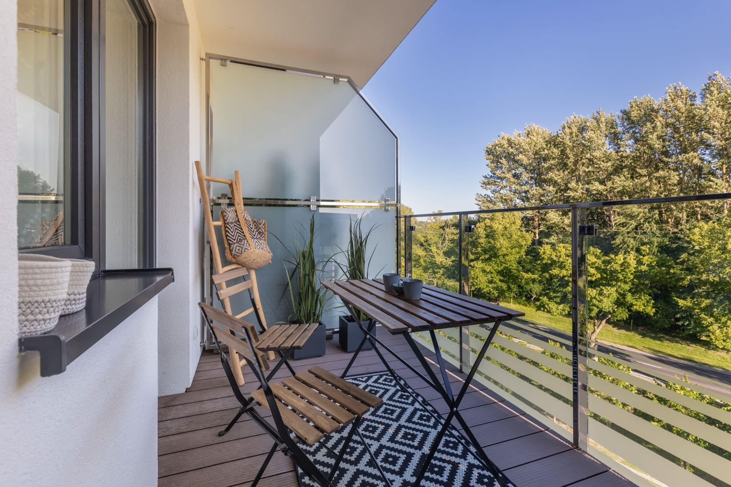 Een balkon met een houten stoel, een kleine tafel en een kleed met dessin.