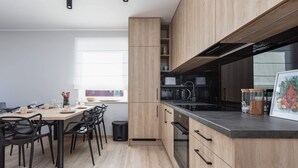 A modern kitchen with wooden cabinets, a black countertop, and a dining area with black chairs. - Bright Apartment with Balcony | Workspace (Kolobrzeg)