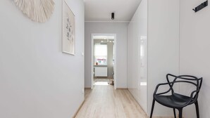 A hallway with a black chair, a framed artwork, and a door leading to a room. - Bright Apartment with Balcony | Workspace (Kolobrzeg)