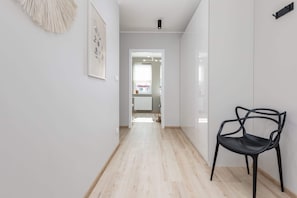 Un pasillo con una silla negra, una obra de arte enmarcada y una puerta que da a una habitación.