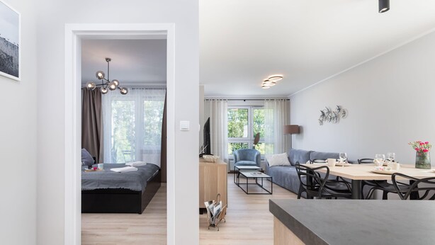 A modern living room with a sofa, a dining table with chairs, a coffee table, and a TV. - Bright Apartment with Balcony | Workspace (Kolobrzeg)