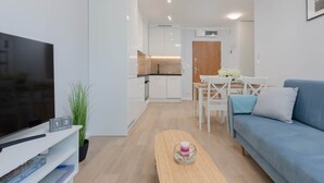 Una sala de estar moderna con televisor de pantalla plana, una mesa de centro de madera, un sofá y un comedor con mesa y sillas blancas.