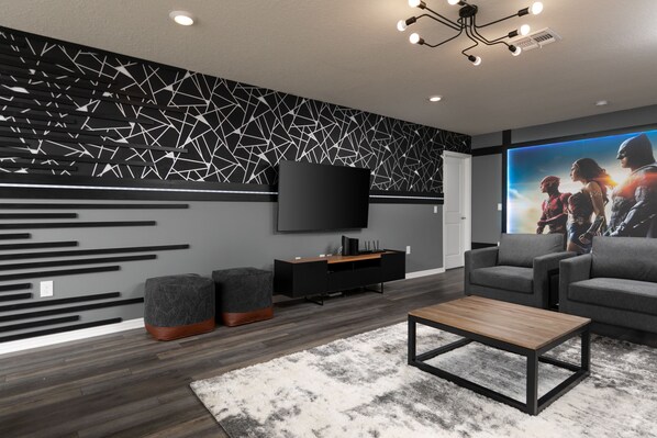 Een moderne woonkamer met een flatscreen televisie, grijze banken, een salontafel en een behang met een patroon.