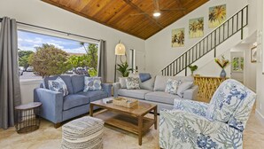 Ampla sala de estar com teto de madeira alto, escada e vista para o exterior.