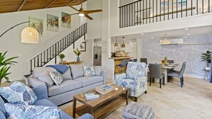 Uma sala de estar espaçosa com pé direito alto, escada e área de cozinha.
