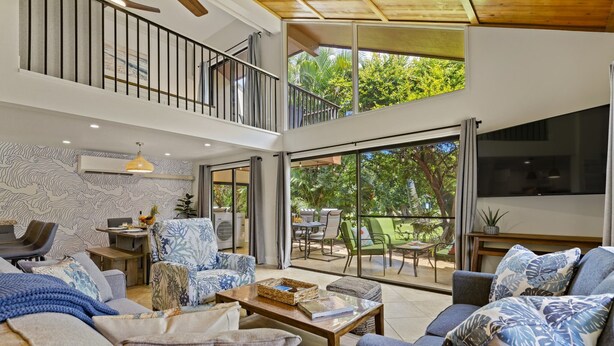 Uma sala de estar ampla com teto alto, uma varanda com mobiliário ao ar livre e grandes janelas que oferecem vista para o exterior.