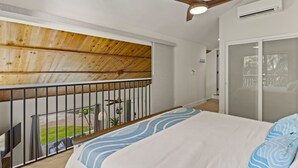 Quarto com cama, ventilador de teto, varanda com guarda-corpo e vista para o exterior.