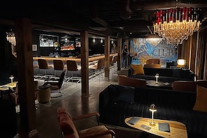 Un salon à l’éclairage tamisé, avec des canapés en cuir, des tables en bois et un bar en arrière-plan.
