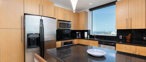 A modern kitchen with wooden cabinets, a stainless steel refrigerator, a microwave, and a large window offering a view.