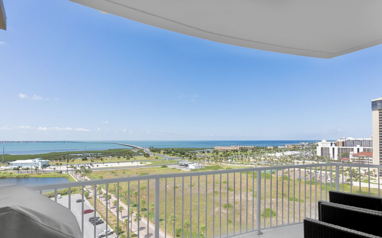 A balcony with a view of the ocean and a distant bridge.