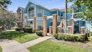 A two-story residential building with a blue exterior, brick pillars, and a covered front porch.