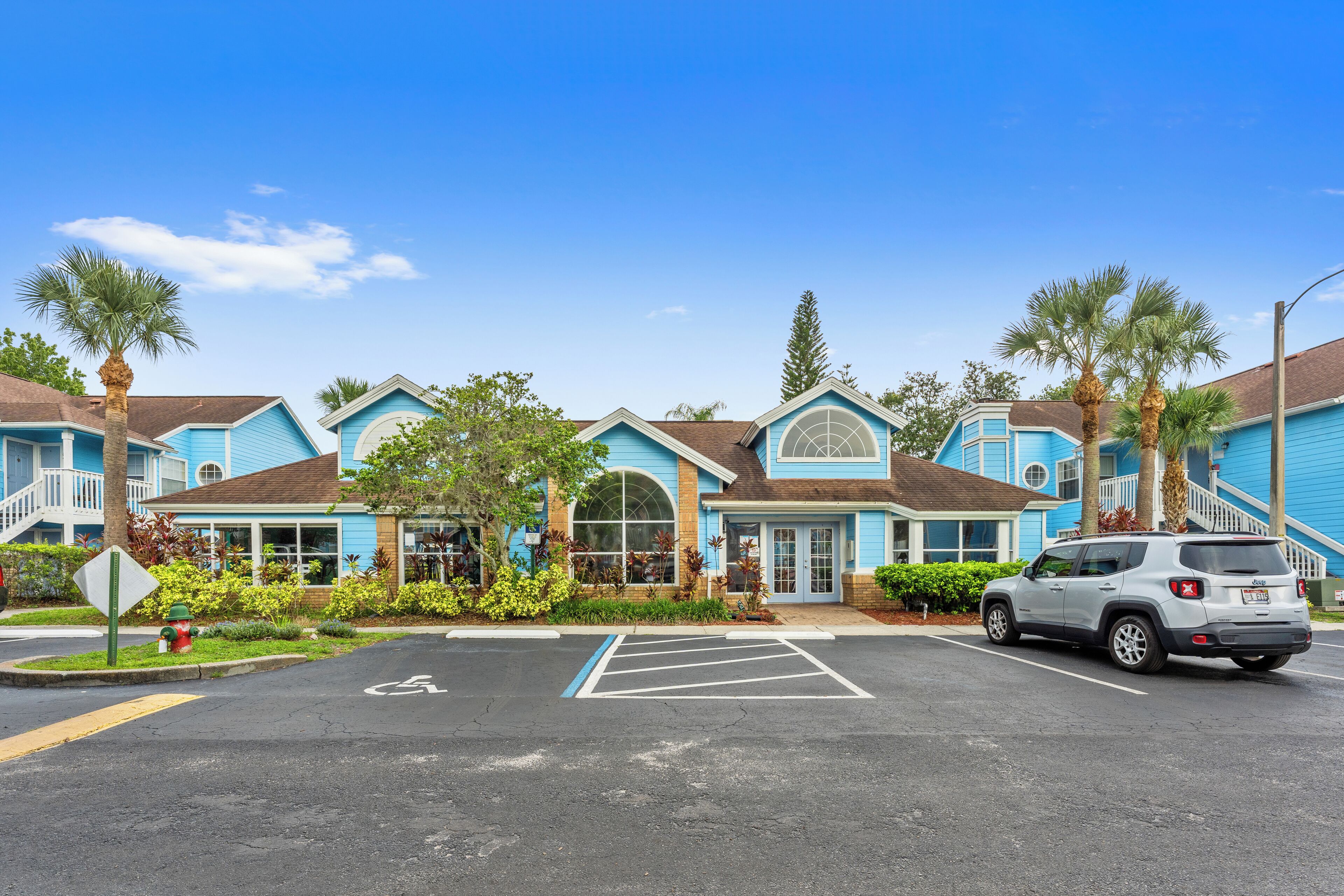 A row of blue buildings with a parking lot in front.