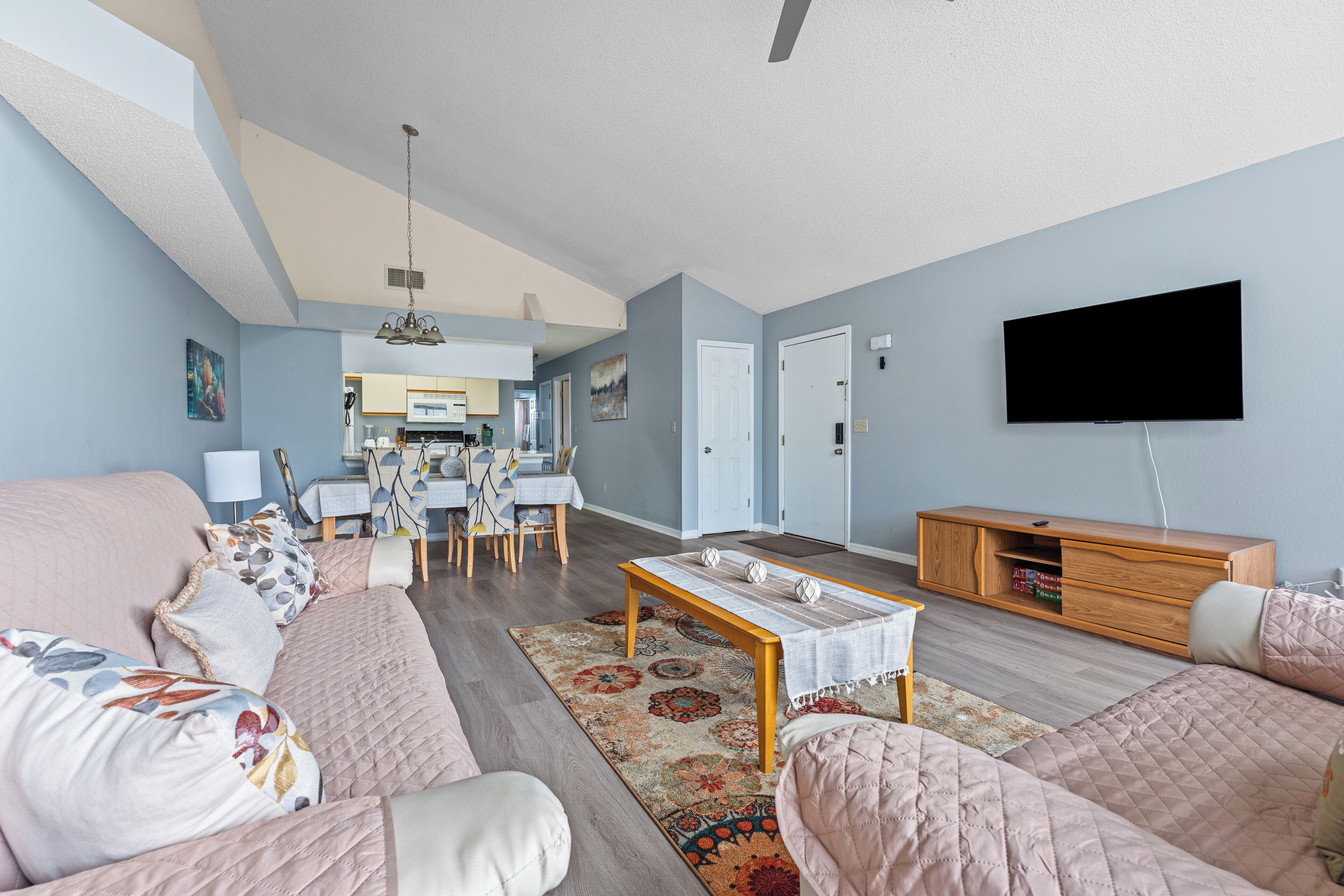 Een ruime woonkamer met een zithoek, een salontafel en een wandgemonteerde flatscreen-televisie.