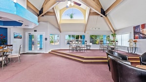 A spacious room with a high ceiling, wooden beams, a skylight, and a dining area with chairs and tables.