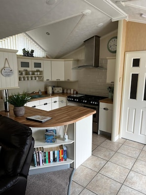 Compact kitchen with a central island, stove, and sink, featuring white cabinetry and a tiled backsplash.