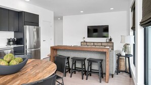 A modern kitchen with dark cabinets, a stainless steel refrigerator, and a wooden dining table with chairs.
