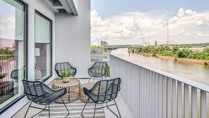 A balcony with a view of a river, two wicker chairs, a small table, and a potted plant.
