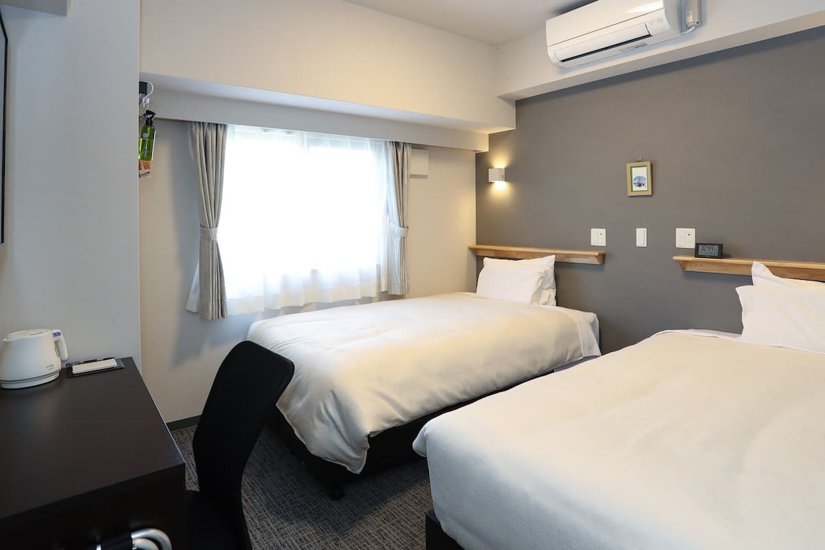 Ein Hotelzimmer mit zwei Betten, einem Schreibtisch mit Wasserkocher, einer Uhr und einem Fenster mit Vorhängen.