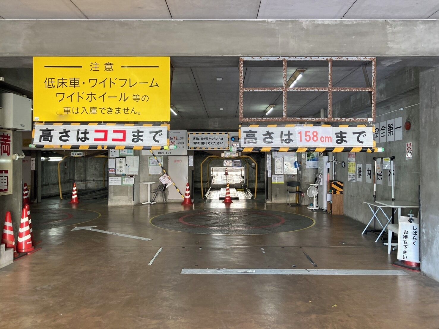 A parking garage entrance with height restriction signs, a yellow caution sign, and a concrete floor with traffic cones.